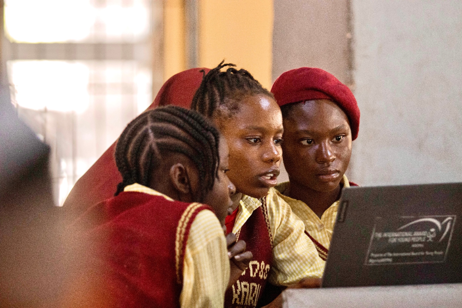Three students clustered around a laptop, working through an exercise together.