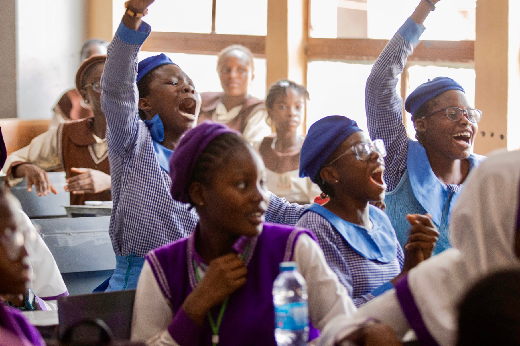 Nigerian secondary-school students cheering with hands raised in class.